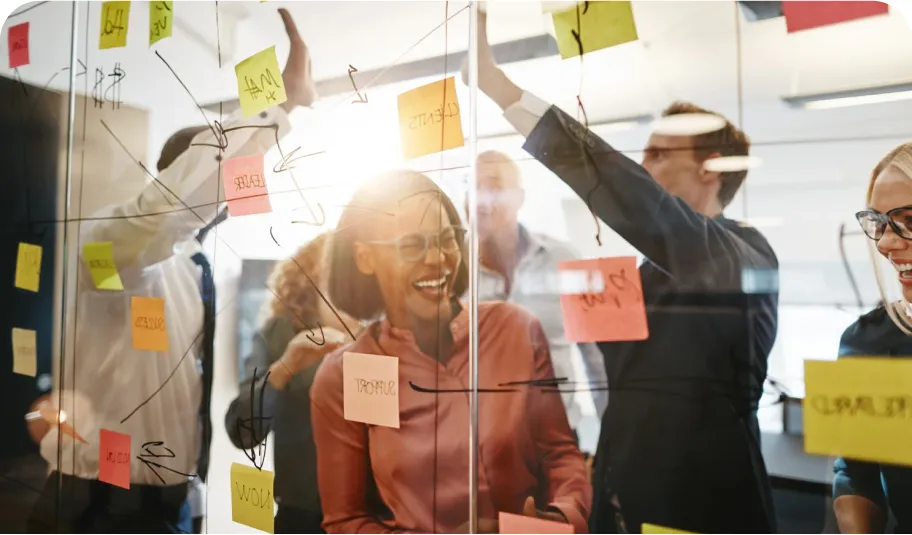 Group of people in glass walled meeting room sticking post-it notes to the walls